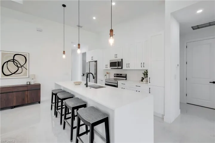 Kitchen featuring stainless steel appliances, a sink, a breakfast bar, white cabinets, and an island with sink