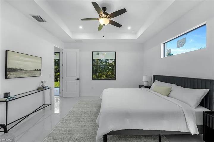Bedroom featuring a tray ceiling, recessed lighting, light marble finish flooring, and a ceiling fan