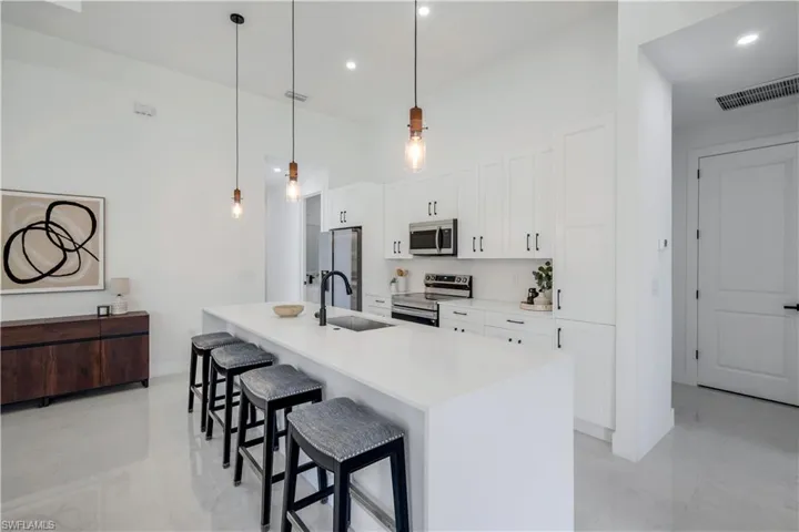 Kitchen with stainless steel appliances, a sink, a breakfast bar, white cabinetry, and a center island with sink
