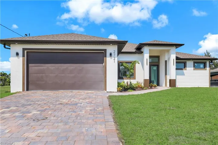 Prairie-style home with a front yard, decorative driveway, stucco siding, and roof with shingles
