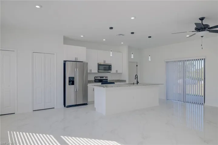 Kitchen featuring a center island with sink, sink, light stone countertops, white cabinetry, and stainless steel appliances