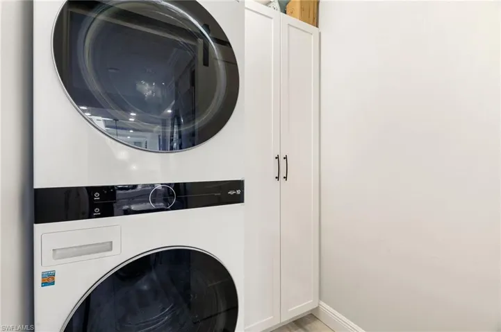Washroom featuring cabinets and stacked washing maching and dryer