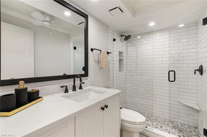 Bathroom featuring ceiling fan, toilet, vanity, a shower with shower door, and ornamental molding