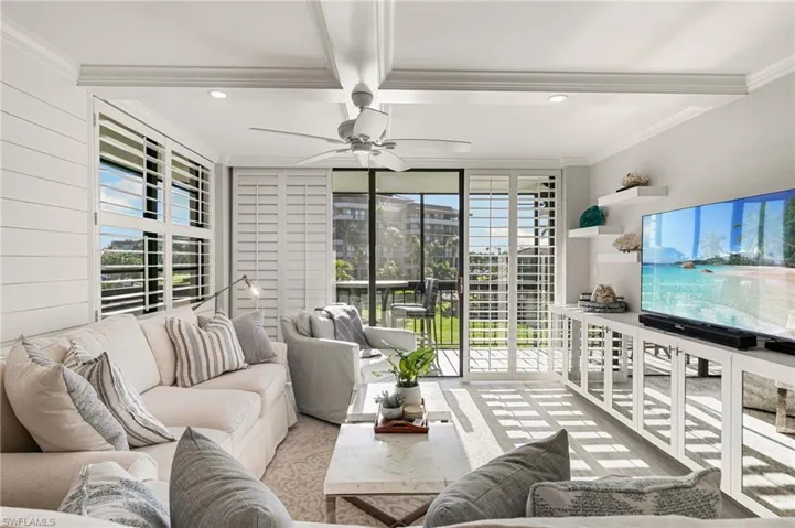 Living room featuring a wealth of natural light, beamed ceiling, ceiling fan, and ornamental molding