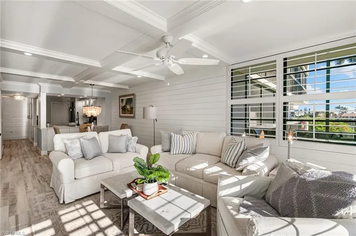 Living room featuring wood walls, coffered ceiling, ceiling fan with notable chandelier, light hardwood / wood-style flooring, and beam ceiling