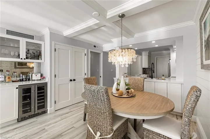 Dining area with coffered ceiling, wine cooler, light hardwood / wood-style flooring, beamed ceiling, and bar area