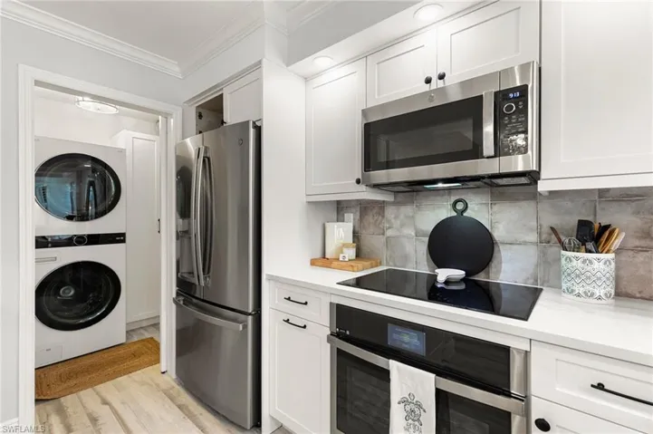 Kitchen with white cabinetry, stacked washing maching and dryer, light hardwood / wood-style flooring, and stainless steel appliances