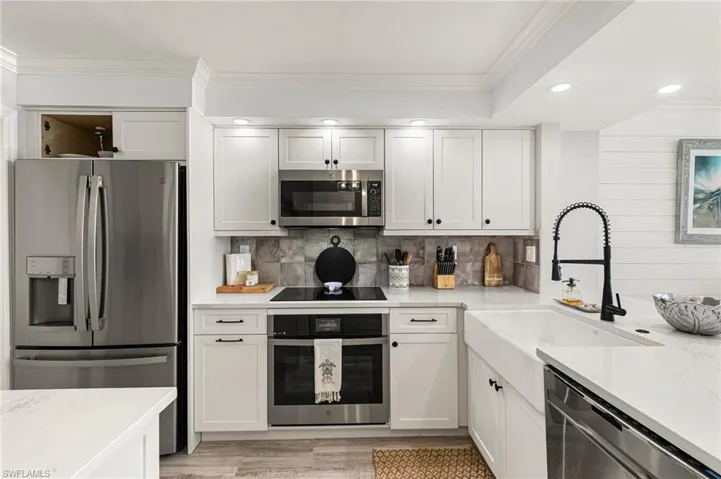 Kitchen featuring backsplash, ornamental molding, stainless steel appliances, sink, and white cabinetry