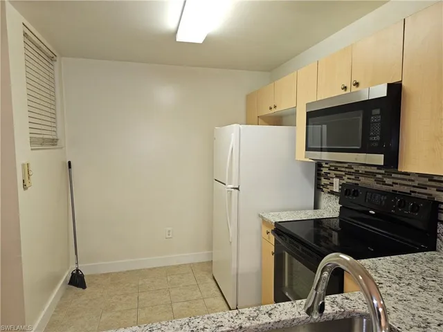Kitchen featuring light brown cabinets, black electric range oven, stainless steel microwave, decorative backsplash, and light stone countertops