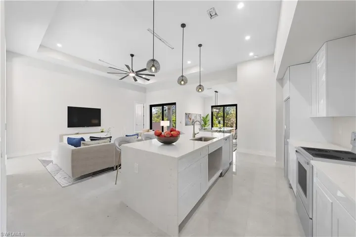 Kitchen featuring white cabinetry, white appliances, light stone countertops, open floor plan, and pendant lighting