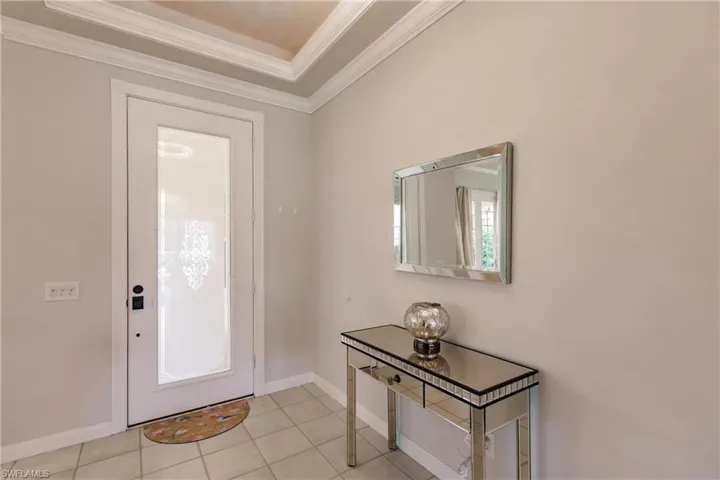 Entrance foyer with ornamental molding, a raised ceiling, and light tile patterned floors