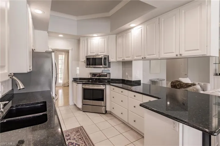 Kitchen with white cabinets, dark stone countertops, light tile patterned floors, crown molding, and appliances with stainless steel finishes