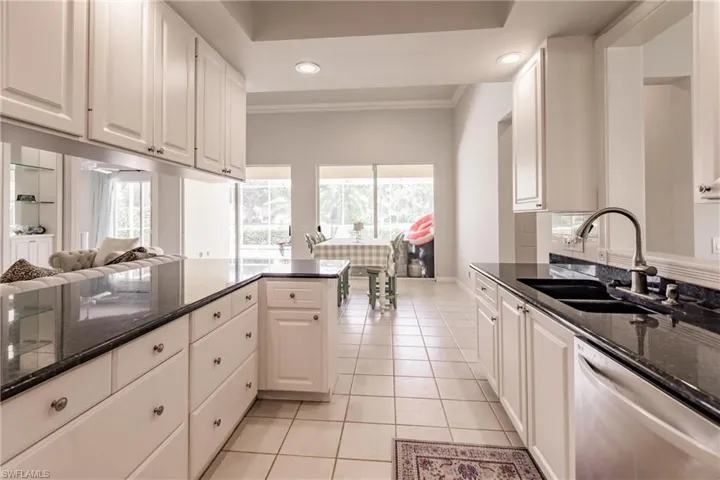 Kitchen featuring dishwasher, light tile patterned floors, sink, white cabinetry, and dark stone countertops
