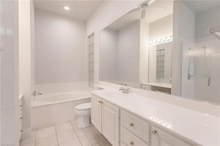 Full bathroom with toilet, plus walk in shower, tile patterned flooring, vanity, and ceiling fan