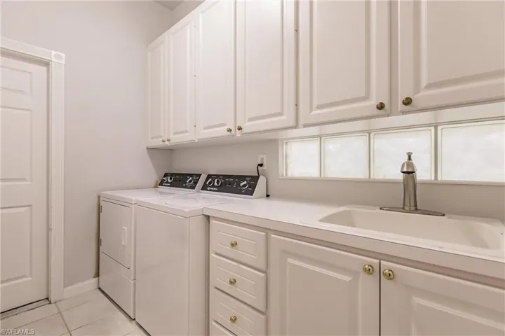 Clothes washing area with light tile patterned flooring, sink, cabinets, and separate washer and dryer