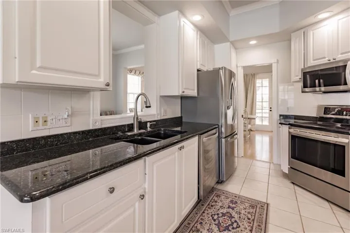 Kitchen with appliances with stainless steel finishes, white cabinetry, dark stone counters, and crown molding