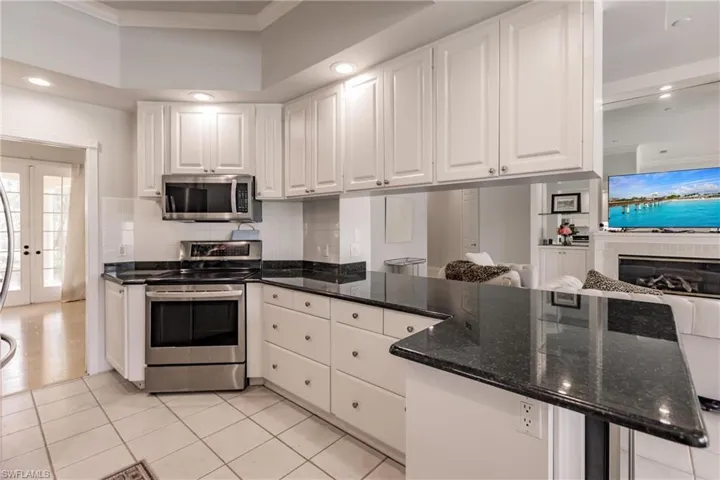 Kitchen featuring tasteful backsplash, stainless steel appliances, white cabinetry, dark stone counters, and light tile patterned flooring