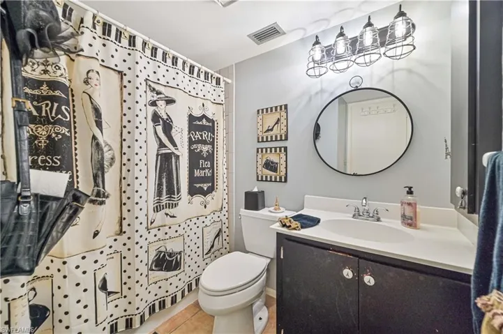 Bathroom featuring tile patterned flooring, toilet, vanity, visible vents, and a shower with curtain