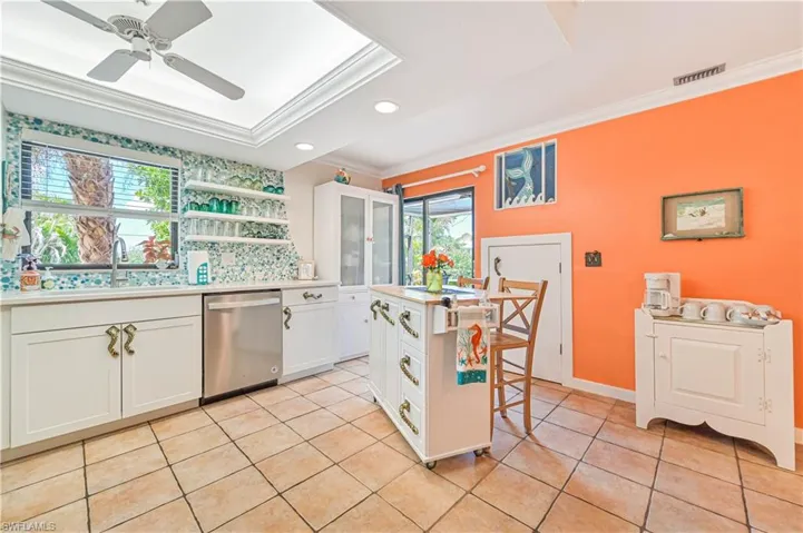 Kitchen featuring stainless steel dishwasher, ornamental molding, white cabinets, a sink, and light tile patterned flooring