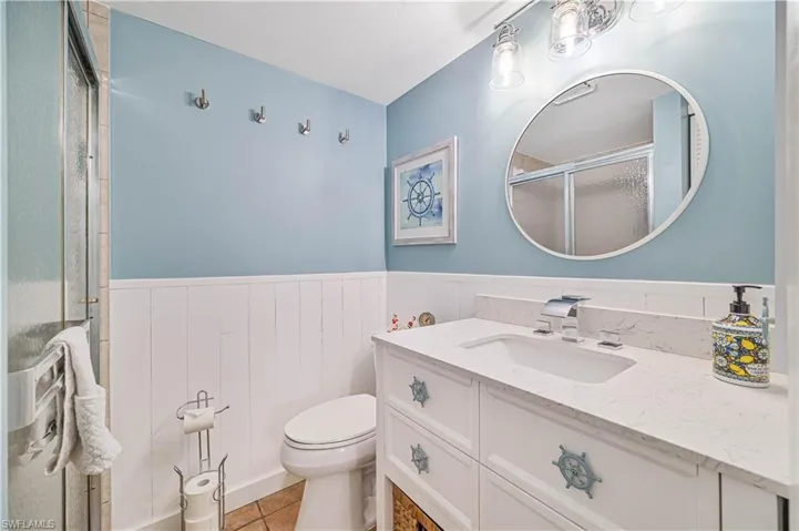 Bathroom with wainscoting, toilet, tile patterned flooring, vanity, and a shower stall