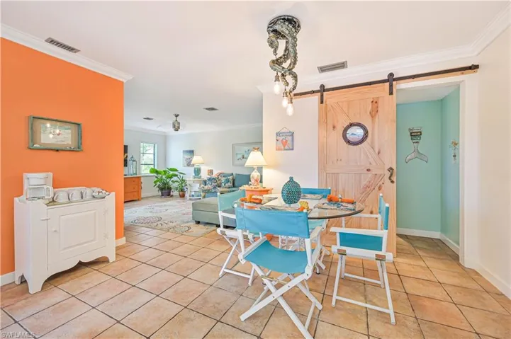 Dining space with ornamental molding, a barn door, light tile patterned flooring, and visible vents