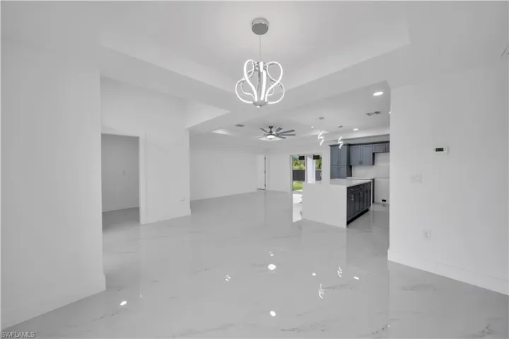 Spacious interior with polished tile flooring, tray ceiling, modern chandelier, recessed lighting, and a built-in kitchen island