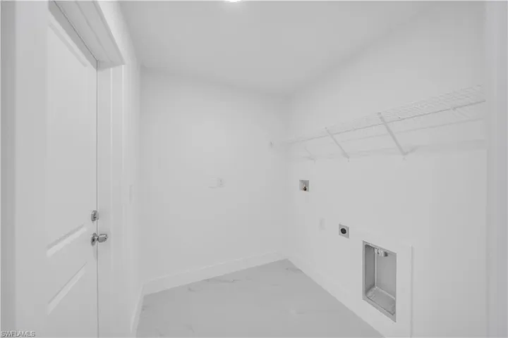 Utility room featuring light-toned flooring, white walls, and a wire shelf