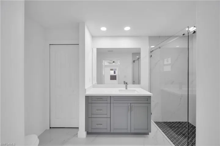Recessed lighting illuminates a gray vanity with an integrated sink and a sleek glass-enclosed shower featuring a black penny tile floor