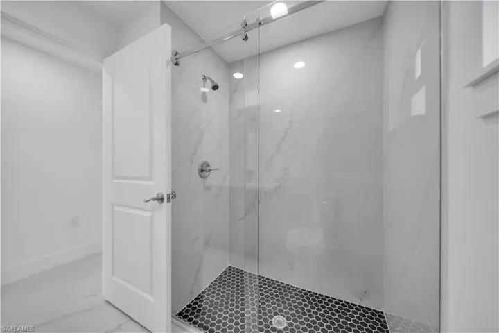 Shower enclosure with a frameless glass door, large format tile walls, and a black hexagonal tile floor