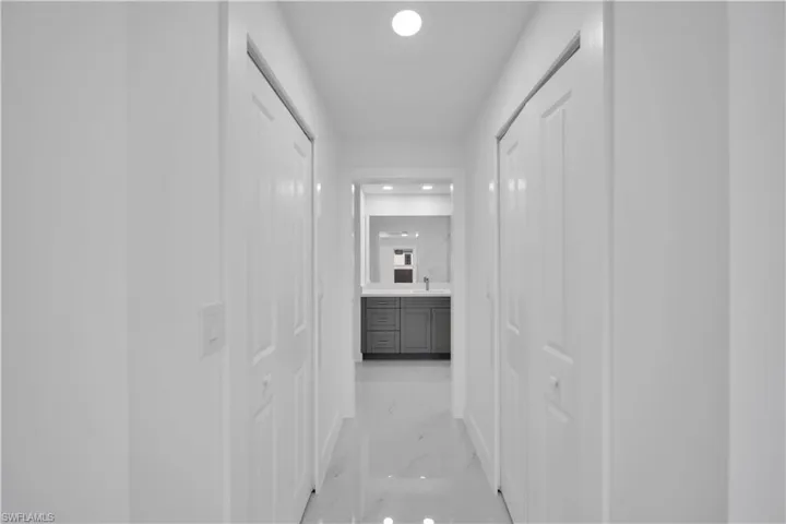 Recessed lighting illuminates a hallway with white walls and bi-fold doors, leading to a bathroom featuring a vanity with dark wood-finish cabinetry