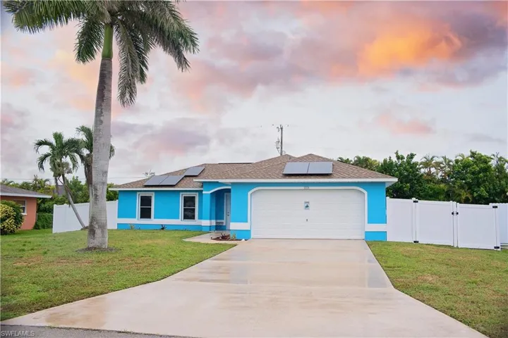 Ranch-style house featuring a shingled roof, solar panels, and driveway