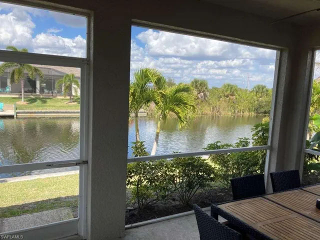 The screened patio offers serene water views, complemented by lush greenery and a bright sky with clouds