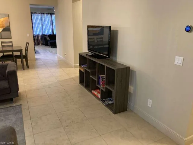 The property features light-colored tiled flooring throughout, a wall-mounted control panel, and a view into an additional room with curtains