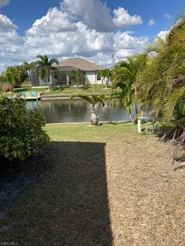 Waterfront property featuring a well-maintained lawn and mature palm trees