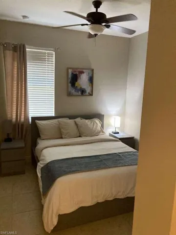 This room features a ceiling fan with integrated lighting, a window with blinds and drapes, and tiled flooring