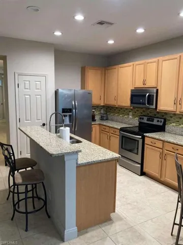 The kitchen features light wood cabinetry, granite countertops, and stainless steel appliances, including a microwave, oven, and refrigerator