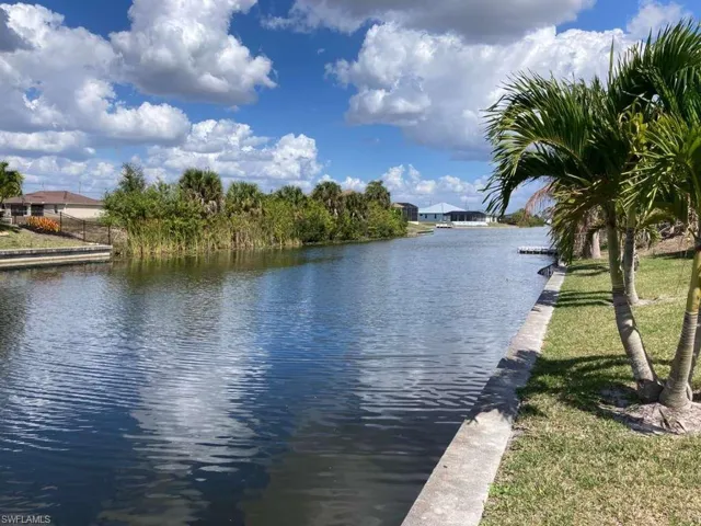 This property offers direct access to a tranquil canal, featuring a manicured lawn area and mature palm trees along the waterfront