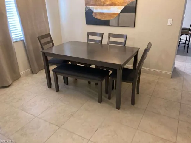 This dining area features neutral-toned tiled flooring, a window with blinds and drapes, and a wall with contemporary artwork