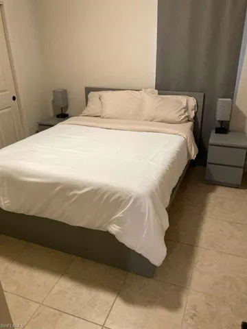 The room features a bed with a gray frame, light-colored walls, and tile flooring