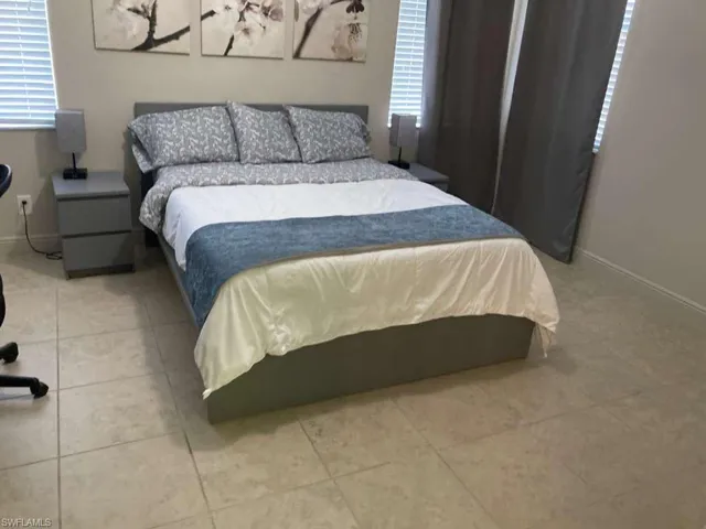 Well-appointed bedroom featuring tile flooring, neutral wall colors, and windows with blinds and drapes