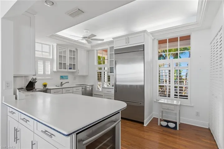 Kitchen with appliances with stainless steel finishes, a raised ceiling, a peninsula, light countertops, and glass insert cabinets