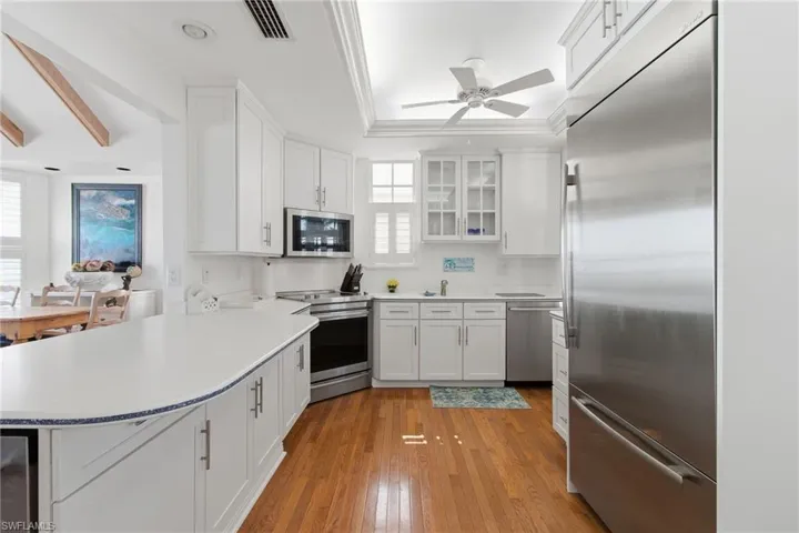 Kitchen with appliances with stainless steel finishes, a peninsula, white cabinets, glass insert cabinets, and light wood-style flooring
