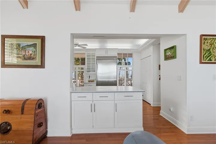 Kitchen with white cabinets, a peninsula, stainless steel built in refrigerator, light wood-style flooring, and glass insert cabinets