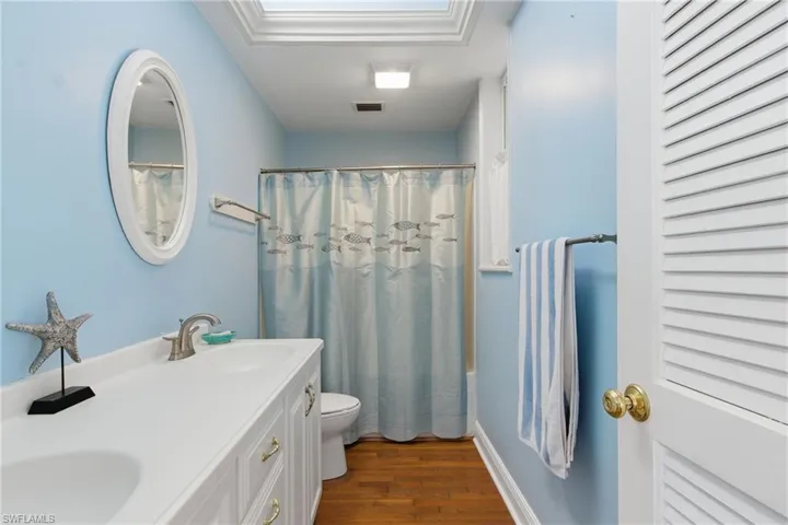 Bathroom with dark wood-type flooring, double vanity, and shower / bath combo with shower curtain