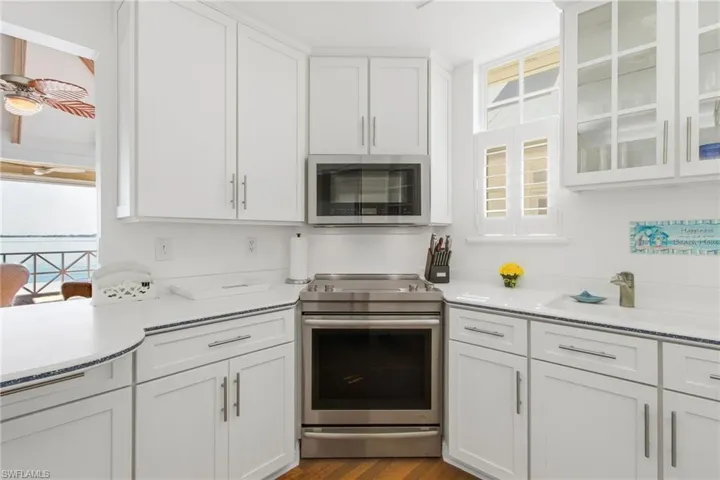 Kitchen featuring stainless steel appliances, white cabinetry, light stone counters, and glass insert cabinets