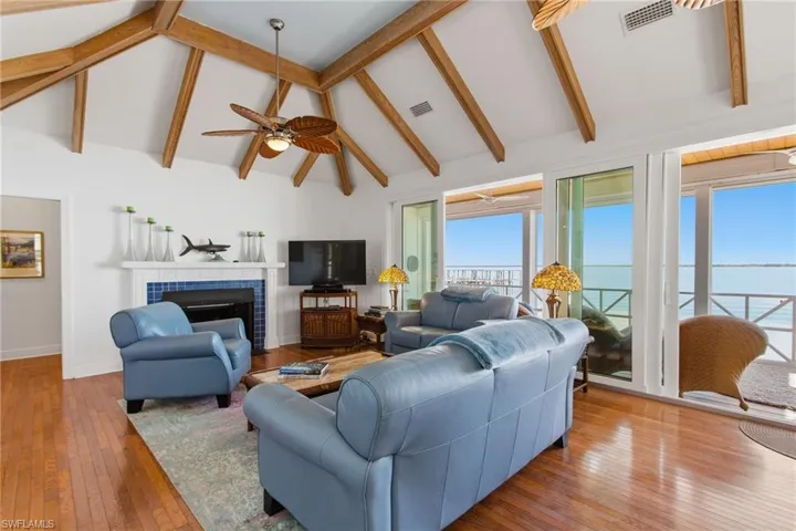 Living room with a tiled fireplace, hardwood / wood-style flooring, high vaulted ceiling, beamed ceiling, and a ceiling fan