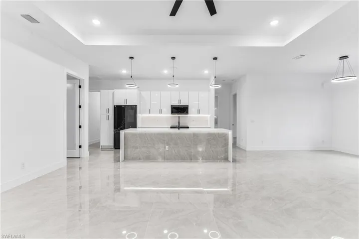 Kitchen featuring a tray ceiling, a kitchen island with sink, pendant lighting, and white cabinets