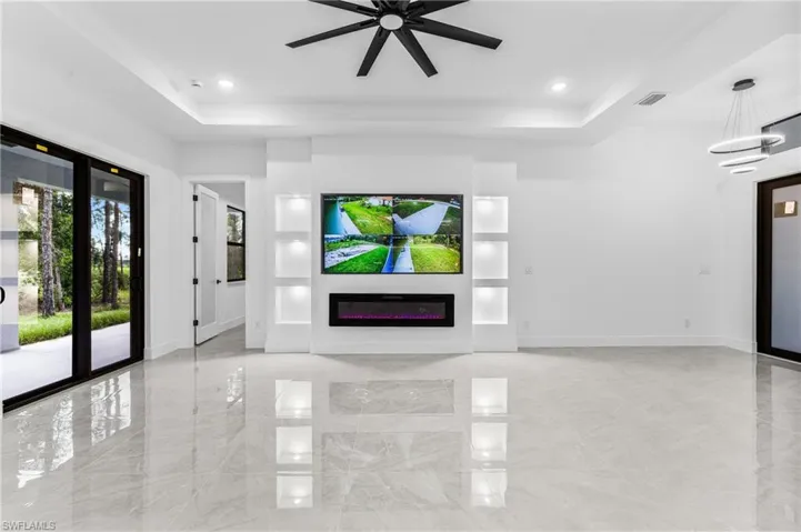 Unfurnished living room featuring ceiling fan with notable chandelier and a tray ceiling