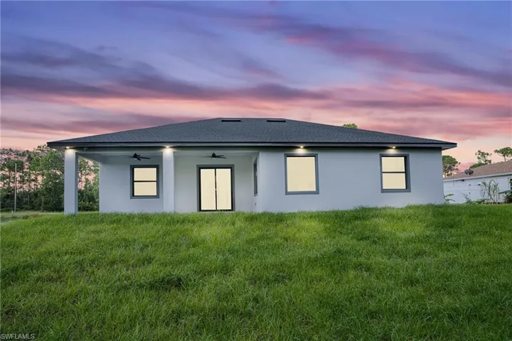 Back house at dusk with ceiling fan and a yard