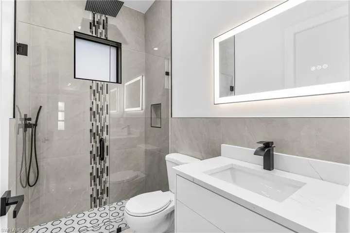 Bathroom featuring vanity, tile walls, a shower with shower door, and toilet
